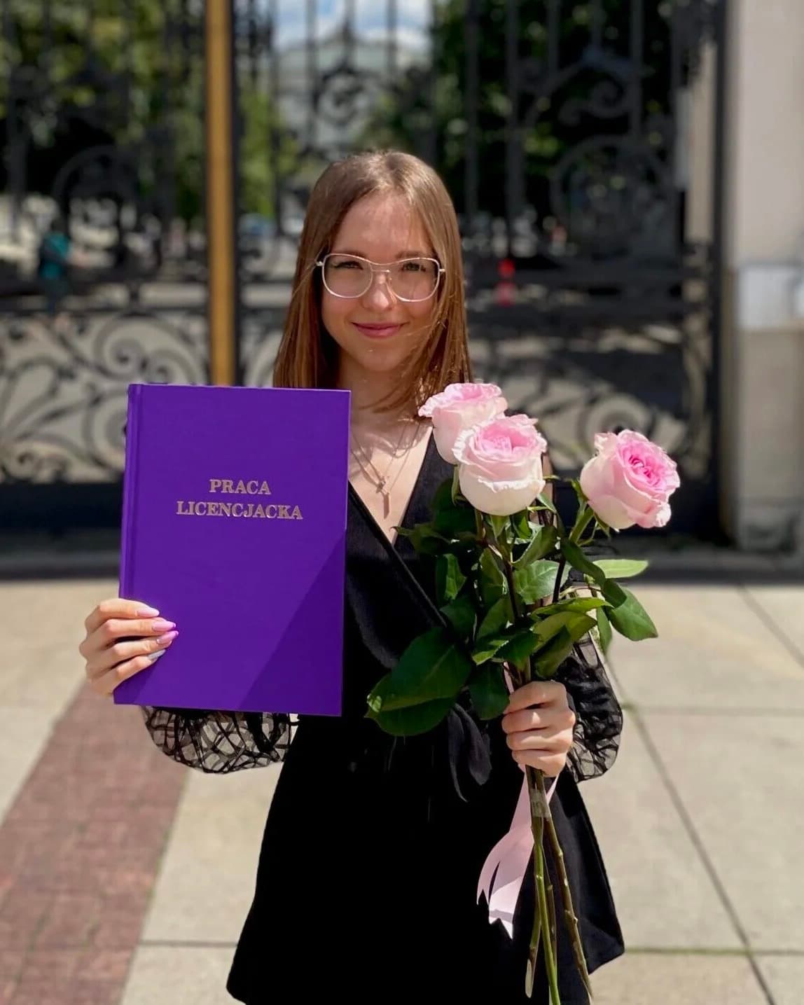 Kinga, nauczycielka angielskiego online, z pracą licencjacką przed bramą Uniwersytetu Warszawskiego